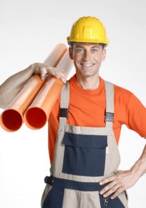 Smiling plumber wearing a hard hat and orange shirt, holding two orange pipes, representing reliable plumbing services for homeowners.