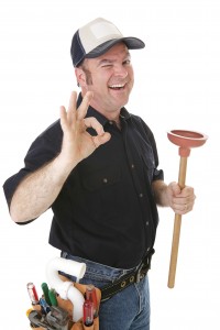 Plumber smiling and giving an "okay" gesture while holding a plunger, representing plumbing services and maintenance for sump pumps.
