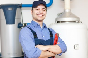 Plumber standing confidently with a wrench, showcasing tank and tankless water heaters in a service environment.