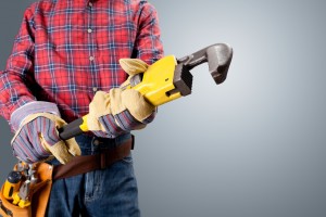 Plumber holding a large pipe wrench, wearing gloves and a plaid shirt, symbolizing professional plumbing services and expertise.