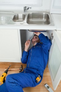 Plumber installing a garbage disposal under a kitchen sink, showcasing professional plumbing services for homeowners.