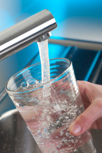 Water pouring from a faucet into a clear glass, emphasizing the importance of clean drinking water and the benefits of a whole-house water filtration system.