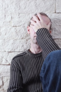 Man with head in hands, expressing distress, against a textured wall, reflecting the urgency and seriousness of addressing gas line leaks for family safety.