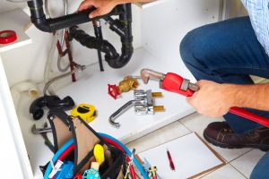 Plumber using tools for drain cleaning under a kitchen sink, showcasing plumbing repairs and maintenance.
