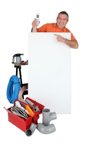 Plumber holding tools and pointing at a blank sign, surrounded by plumbing equipment and materials, emphasizing professional plumbing services and annual drain cleaning.