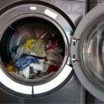 Washing machine door open showing a mix of wet, wrinkled clothing, illustrating potential causes of odor and clogs in laundry appliances.