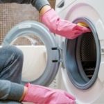 Person wearing pink gloves cleaning the interior of a washing machine, addressing odor issues related to clogs and dirty water, relevant to plumbing maintenance and services by The Plumbing Dr.