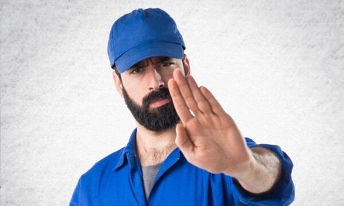 Man in blue work uniform and cap signaling "stop," emphasizing the importance of professional plumbing services.