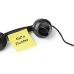 Black telephone receiver with a sticky note reading "Call a Plumber," emphasizing the importance of professional plumbing services for water heater installations.