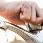 Hand turning off a faucet, emphasizing water conservation and eco-friendly plumbing practices.