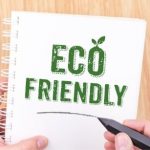 Hand holding a marker writing "Eco Friendly" on a notebook, emphasizing sustainable plumbing practices and water conservation.