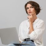 Woman contemplating while using a laptop, representing the need for emergency plumbing services and decision-making in plumbing issues.