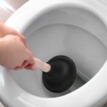 Person using a black plunger in a toilet, illustrating DIY plumbing techniques for resolving clogs and sewage backups.