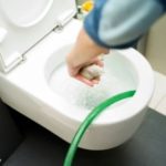 Person using a green hose to flush a toilet, demonstrating plumbing maintenance techniques related to emergency plumbing services.