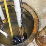 Sump pump installation in basement with water, measuring tape, and pipes, highlighting importance of backup sump pumps for flood prevention.