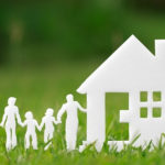 Paper cutouts of a family standing beside a house on green grass, symbolizing eco-friendly home solutions and community.