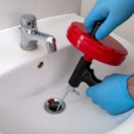 Person using a drain snake tool to unclog a sink, emphasizing DIY drain cleaning methods relevant to plumbing services.
