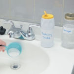 Person pouring baking soda into a sink, alongside labeled containers of baking soda and vinegar, illustrating DIY drain cleaning methods relevant to plumbing services offered by The Plumbing Dr.