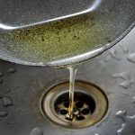 Grease pouring from a pan into a kitchen sink drain, illustrating improper disposal practices that can lead to plumbing clogs and sewer line issues.
