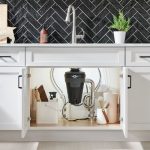 Garbage disposal unit installed under a kitchen sink, showcasing plumbing connections and storage items, relevant to garbage disposal repair and maintenance services offered by The Plumbing Dr.