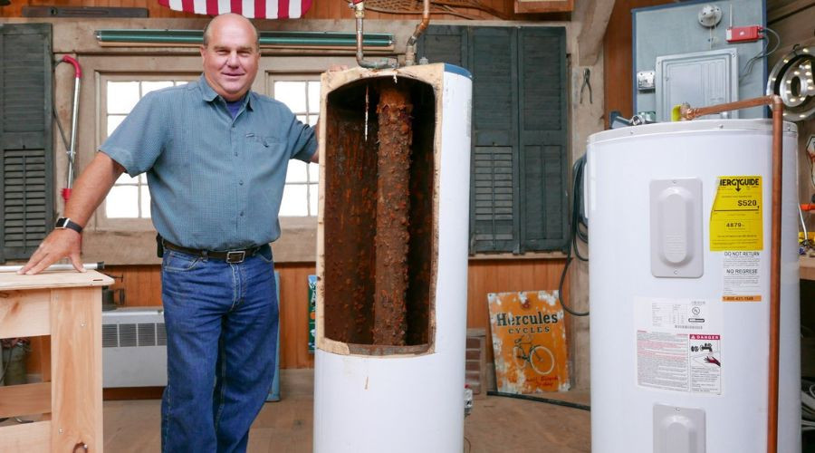 Man standing next to a damaged water heater, showcasing rust and corrosion, emphasizing signs of water heater failure in a plumbing maintenance context.