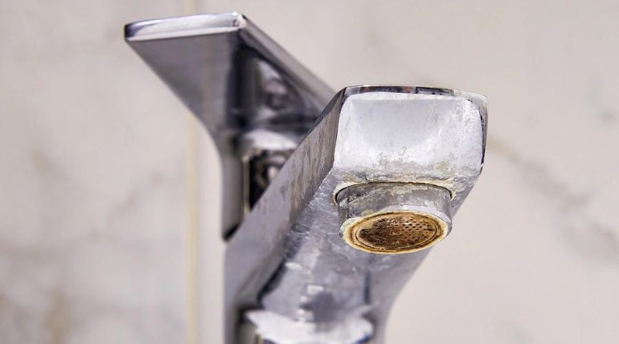 Close-up of a tarnished bathroom faucet showing mineral buildup, highlighting the need for plumbing maintenance to prevent issues during the holiday season.