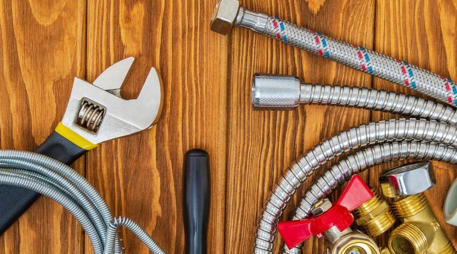 Plumbing tools including a wrench, flexible hoses, and various fittings on a wooden surface, emphasizing plumbing maintenance and repair.