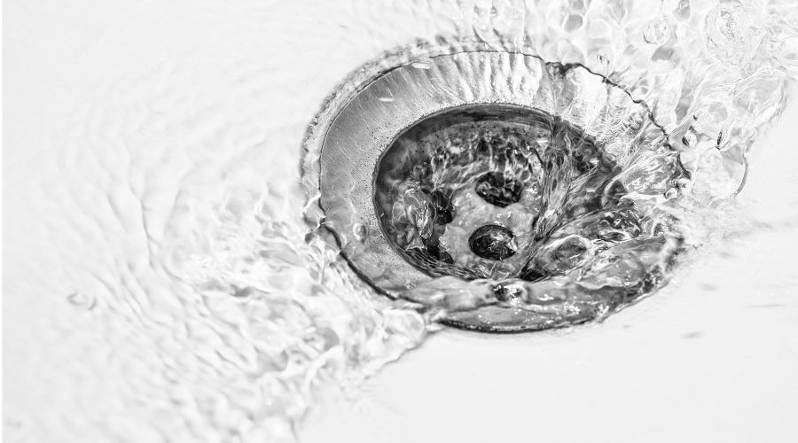 Close-up of a drain with water swirling around, illustrating the importance of professional drain cleaning techniques discussed in plumbing service guide.
