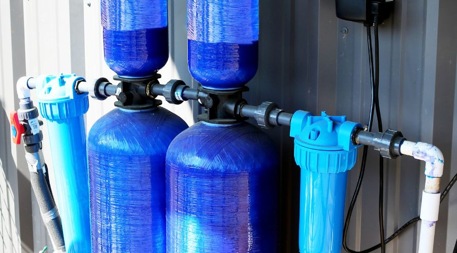 Whole house water filtration system with blue tanks and connected pipes, illustrating water purification for improved home water quality.