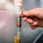 Hand adjusting a gas line connection with visible steam, illustrating gas line repair and safety measures related to gas leaks.