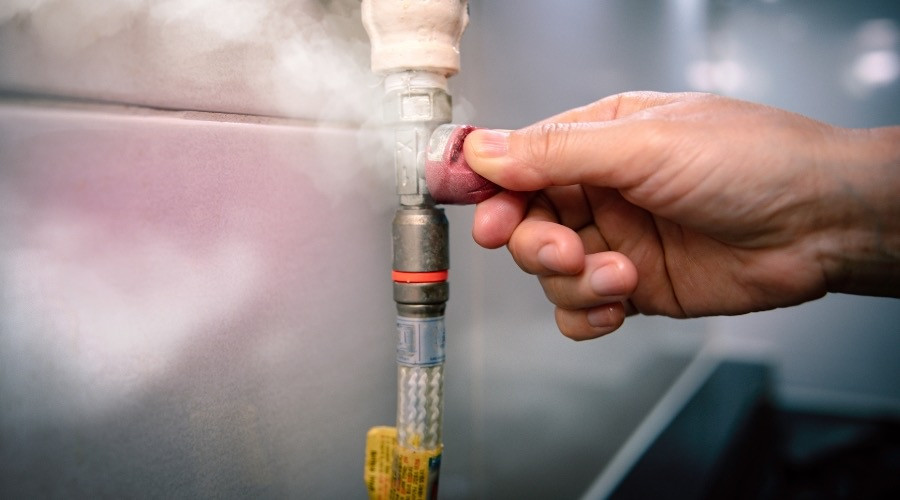 Hand adjusting a gas valve on a plumbing pipe, with steam visible, illustrating gas leak safety response in plumbing maintenance.