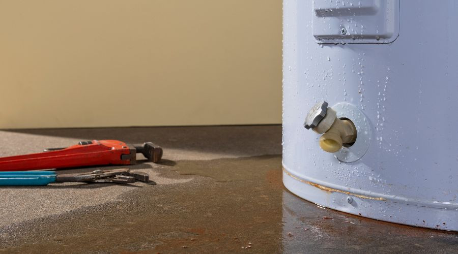 Water heater with visible valve and plumbing tools on wet floor, indicating potential leaks and need for replacement.