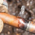 Leaking copper pipe with water spraying from a small hole, indicating a potential plumbing issue, relevant to water leak detection and repair services offered by The Plumbing Dr.