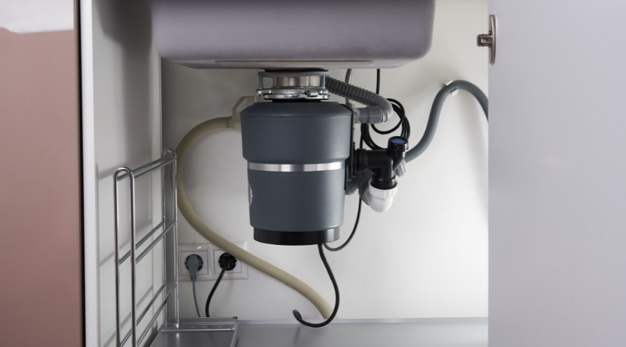 Garbage disposal unit installed under kitchen sink, highlighting plumbing connections and potential signs of wear or malfunction.