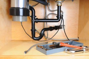 Garbage disposal plumbing connections showing discharge pipe, hose, and tools for maintenance under a kitchen sink.