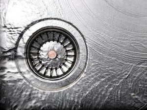 Garbage disposal drain with water flowing, highlighting potential leakage issues in kitchen plumbing.